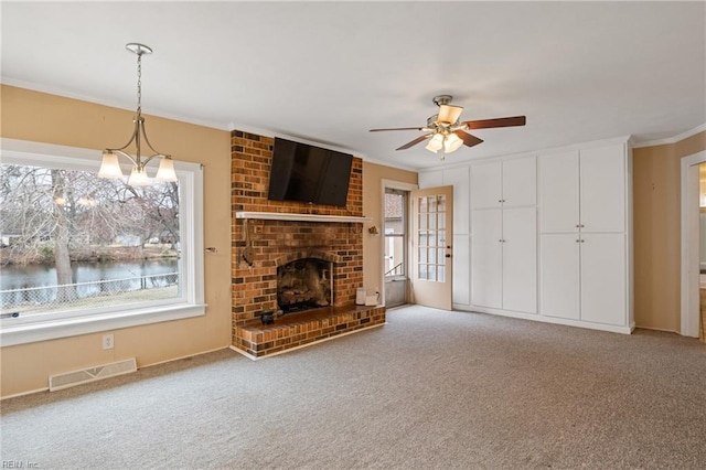 unfurnished living room with visible vents, a brick fireplace, crown molding, ceiling fan, and carpet flooring