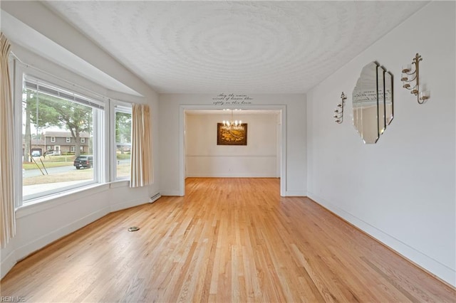 empty room with light wood-type flooring, baseboards, a notable chandelier, and a textured ceiling