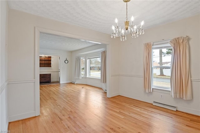 unfurnished dining area with baseboards, light wood-style flooring, a notable chandelier, a textured ceiling, and a baseboard radiator