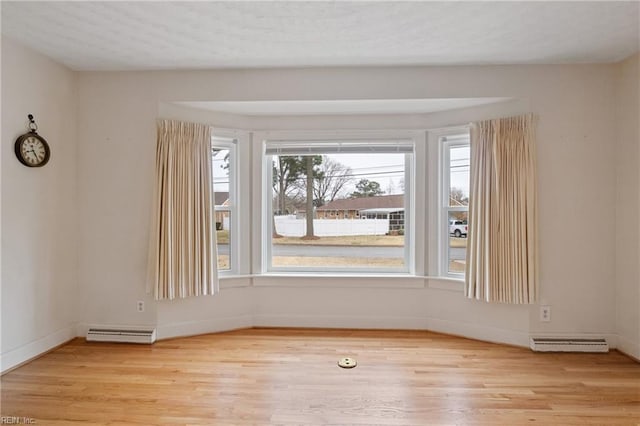 spare room featuring visible vents, wood finished floors, baseboards, and a baseboard radiator