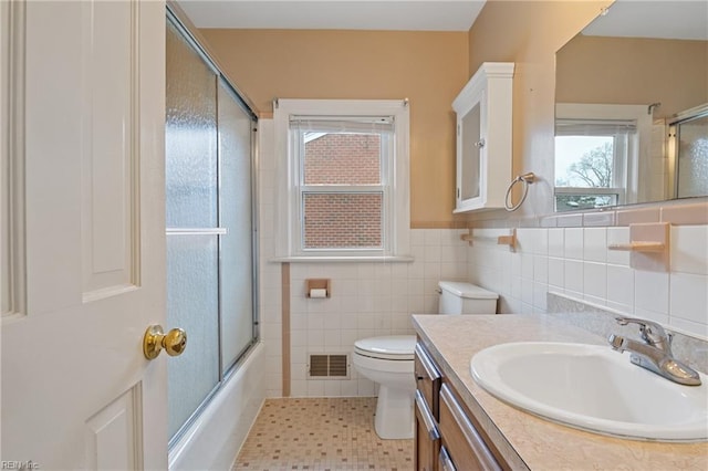 full bath with visible vents, toilet, tile walls, bath / shower combo with glass door, and vanity