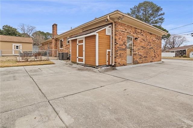 exterior space featuring brick siding, cooling unit, a chimney, and fence