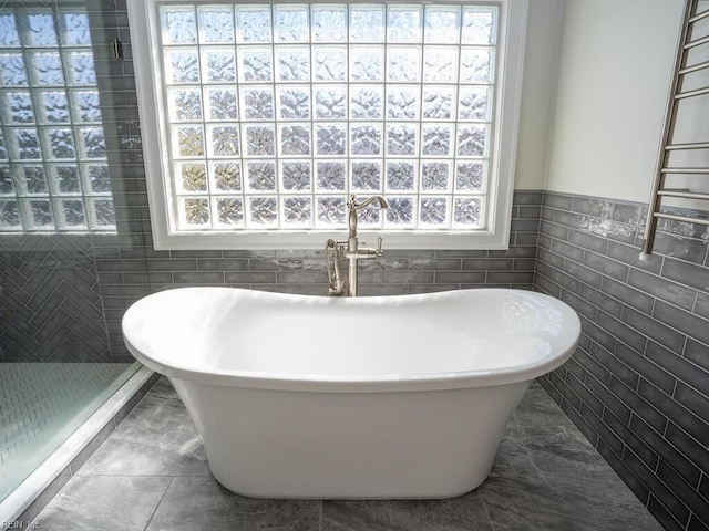 bathroom featuring tile walls, a healthy amount of sunlight, and a freestanding bath