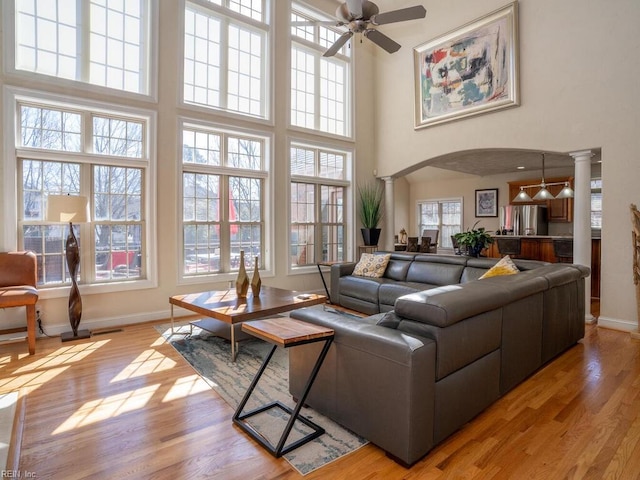 living area with arched walkways, light wood finished floors, a ceiling fan, and decorative columns