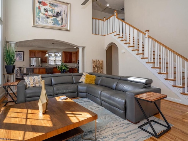 living room featuring arched walkways, light wood finished floors, ceiling fan, stairs, and ornate columns