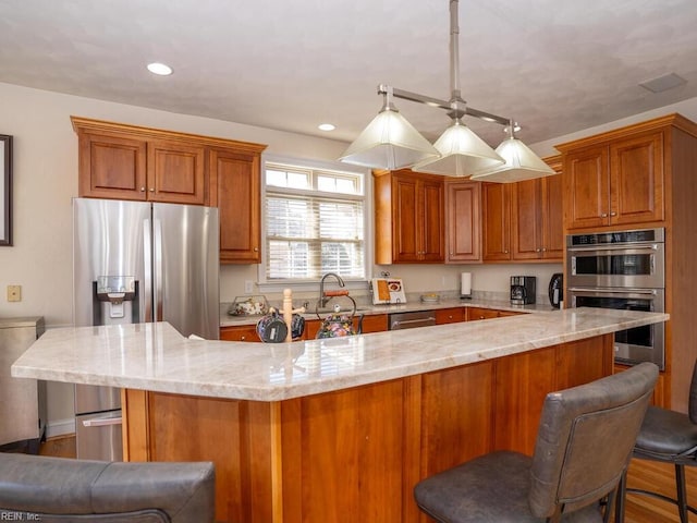 kitchen featuring a breakfast bar area, light stone counters, appliances with stainless steel finishes, brown cabinetry, and a sink