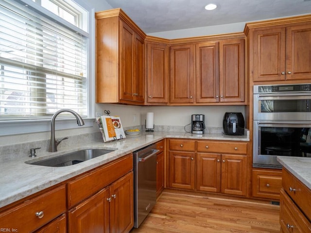 kitchen with light wood-type flooring, light stone counters, brown cabinets, appliances with stainless steel finishes, and a sink