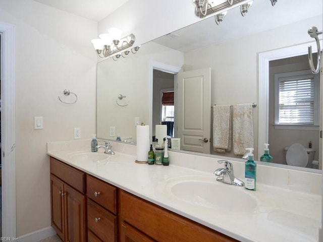 full bath with double vanity, a chandelier, toilet, and a sink