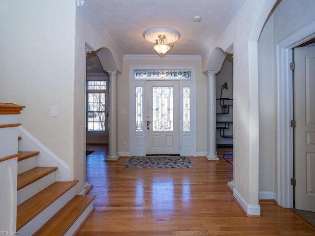 foyer entrance with baseboards, light wood finished floors, decorative columns, arched walkways, and ornamental molding