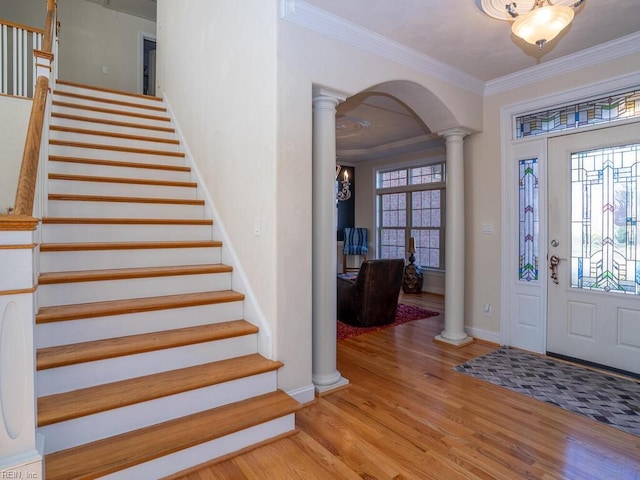 entryway featuring a wealth of natural light, wood finished floors, arched walkways, crown molding, and ornate columns