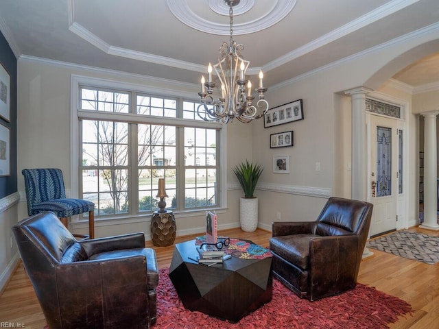 living area featuring a notable chandelier, wood finished floors, arched walkways, crown molding, and decorative columns