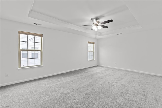carpeted empty room featuring visible vents, baseboards, a raised ceiling, and ceiling fan