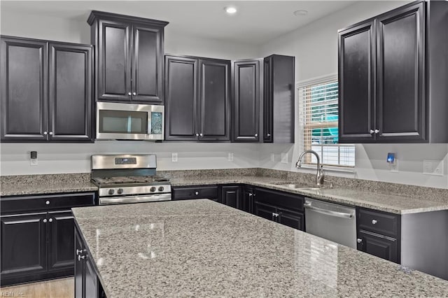 kitchen with light stone counters, a sink, stainless steel appliances, and dark cabinets