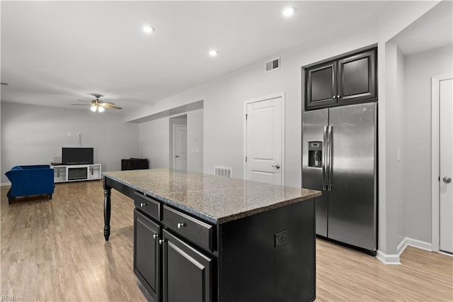 kitchen featuring visible vents, a kitchen island, light wood-type flooring, stainless steel refrigerator with ice dispenser, and dark cabinets