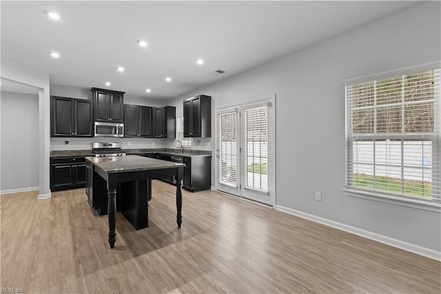 kitchen featuring dark cabinetry, visible vents, light wood finished floors, stainless steel appliances, and a center island