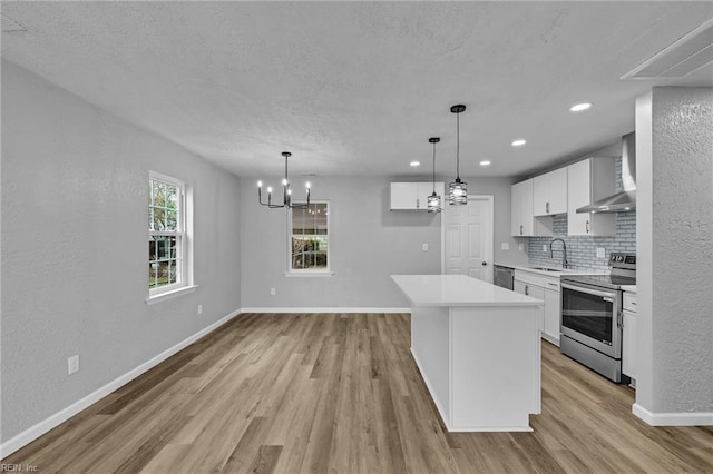 kitchen with baseboards, decorative backsplash, stainless steel appliances, wall chimney exhaust hood, and a sink