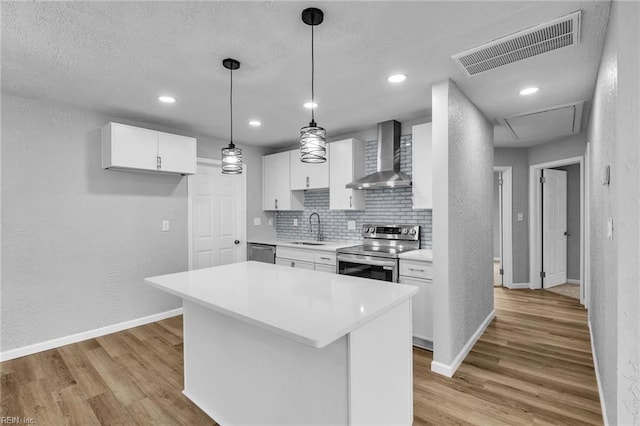 kitchen with visible vents, light wood-style flooring, stainless steel appliances, wall chimney exhaust hood, and a sink