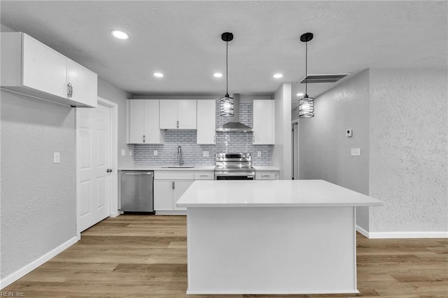 kitchen featuring a textured wall, appliances with stainless steel finishes, light wood-style flooring, and wall chimney range hood