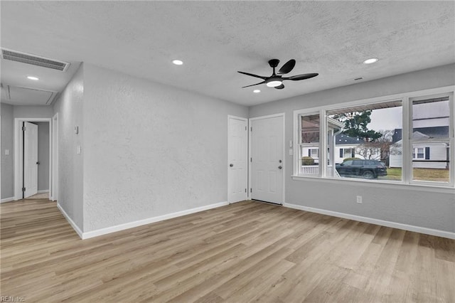 spare room featuring visible vents, light wood finished floors, and a textured wall