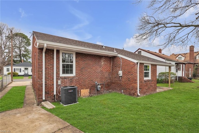 back of house with central air condition unit, a yard, brick siding, and fence