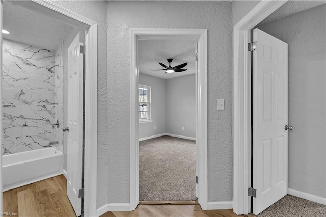 hallway with wood finished floors, a textured wall, baseboards, and a textured ceiling