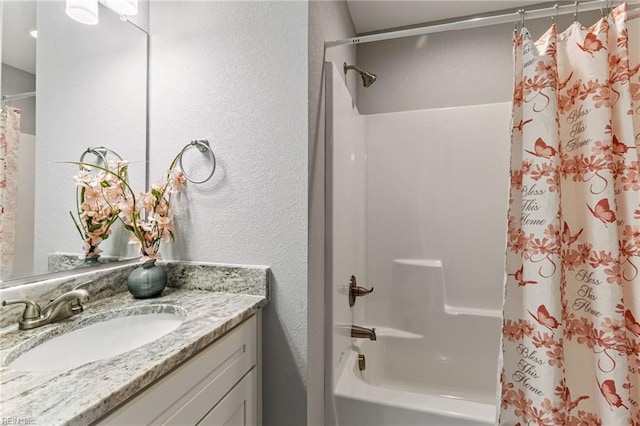 bathroom with vanity, shower / bathtub combination with curtain, and a textured wall