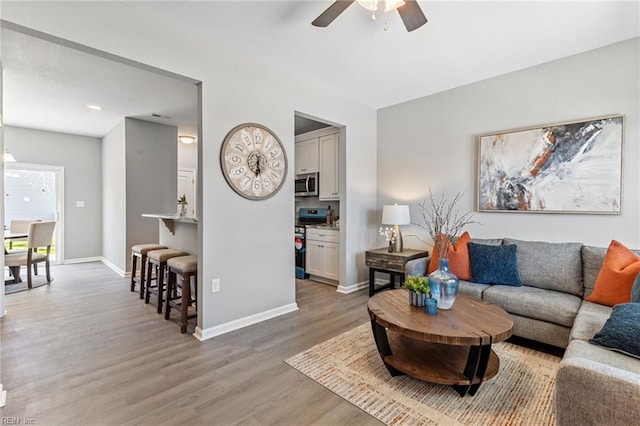 living area with light wood-type flooring, baseboards, and ceiling fan