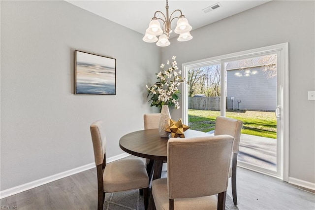 dining space featuring wood finished floors, visible vents, baseboards, and a chandelier