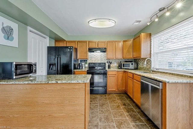 kitchen featuring light stone countertops, a sink, black appliances, under cabinet range hood, and tasteful backsplash