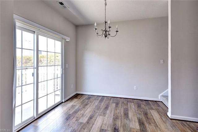 unfurnished dining area featuring an inviting chandelier, wood finished floors, baseboards, and visible vents