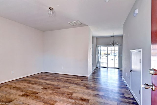 spare room featuring baseboards, visible vents, wood-type flooring, and an inviting chandelier