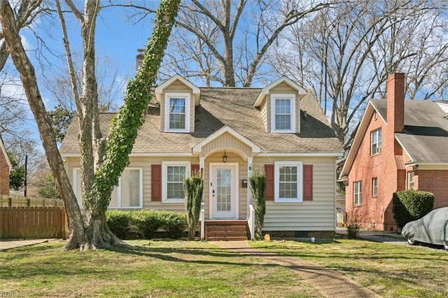 cape cod-style house with a shingled roof, a front lawn, and fence