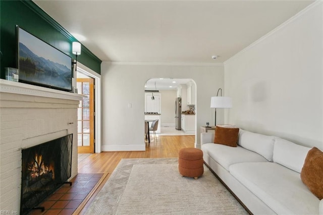 living room with crown molding, baseboards, light wood-type flooring, a fireplace, and arched walkways