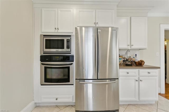 kitchen featuring light tile patterned flooring, white cabinets, appliances with stainless steel finishes, and crown molding