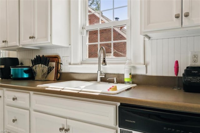 kitchen featuring dishwashing machine, white cabinetry, and a sink