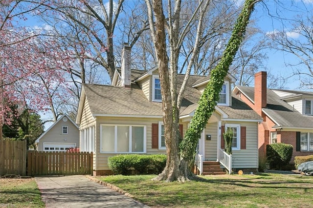 new england style home with driveway, a front yard, a chimney, and fence