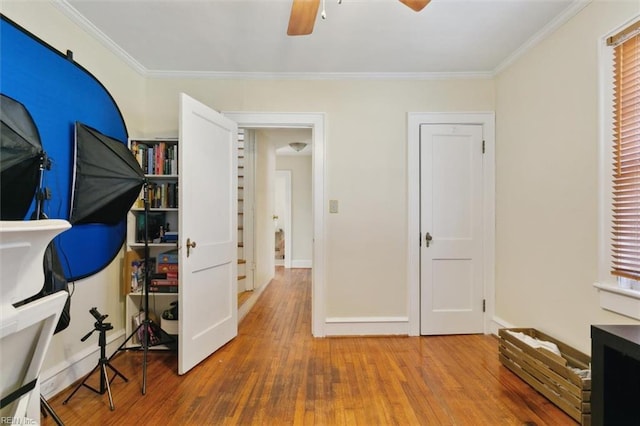 interior space with baseboards, crown molding, a ceiling fan, and hardwood / wood-style flooring