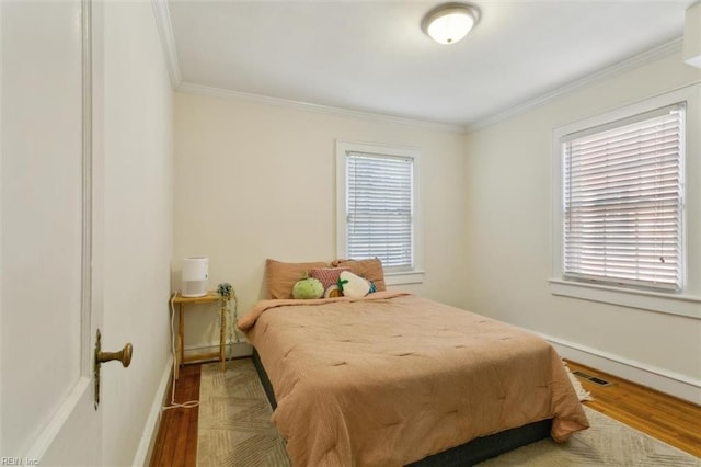 bedroom with wood finished floors, baseboards, multiple windows, and ornamental molding