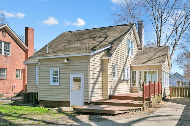 back of house with fence, a wooden deck, central AC, roof with shingles, and a chimney