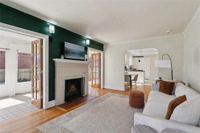 living area featuring light wood finished floors, baseboards, ornamental molding, a fireplace, and arched walkways