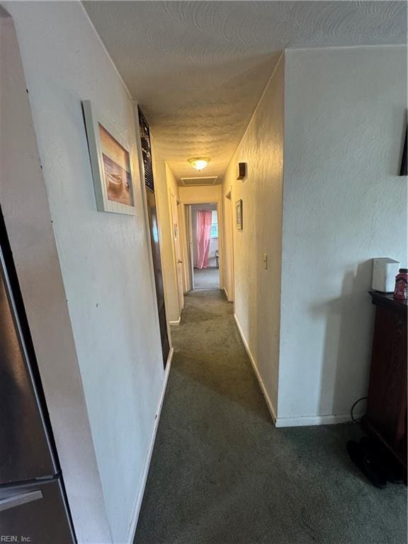 hallway with a textured wall, a textured ceiling, baseboards, and carpet floors