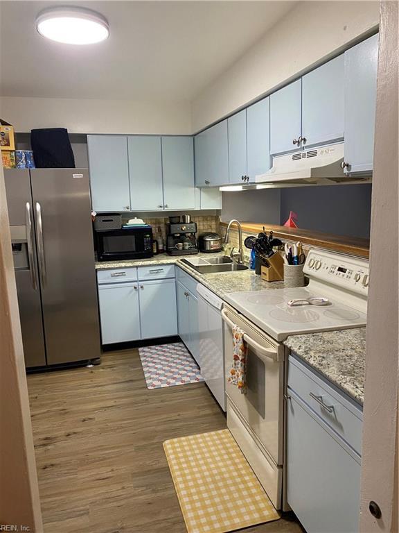 kitchen with under cabinet range hood, white appliances, light wood-type flooring, and a sink