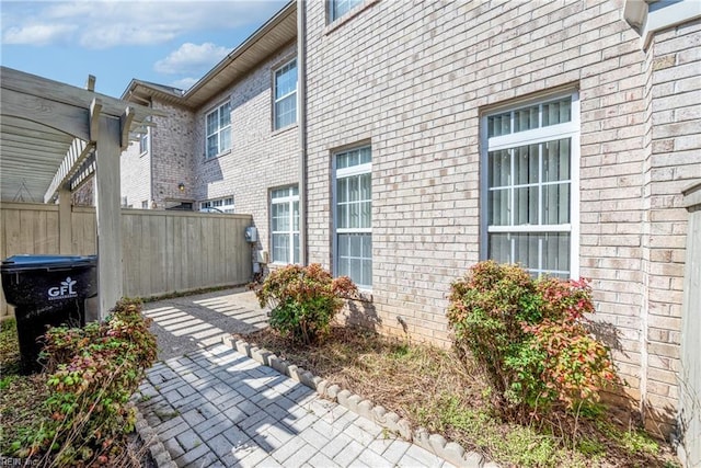 view of side of home with brick siding, a patio area, a pergola, and fence