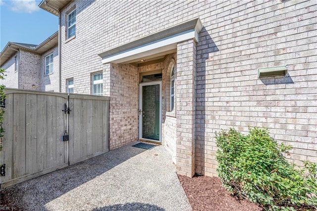 doorway to property featuring fence, brick siding, and a gate