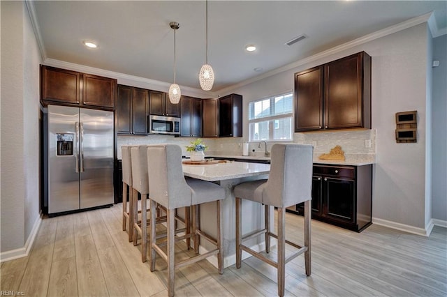 kitchen with light wood finished floors, a kitchen breakfast bar, stainless steel appliances, visible vents, and dark brown cabinets