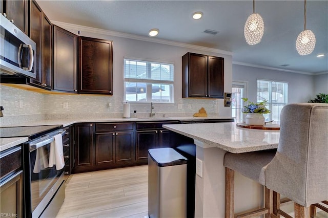 kitchen featuring visible vents, a kitchen bar, stainless steel appliances, a sink, and a wealth of natural light