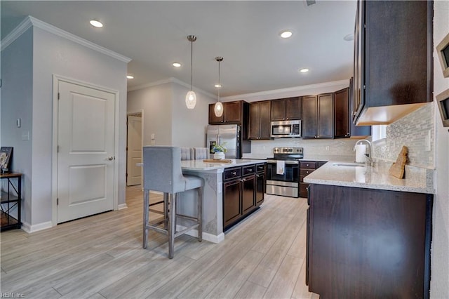 kitchen with decorative backsplash, appliances with stainless steel finishes, dark brown cabinetry, a sink, and a breakfast bar area