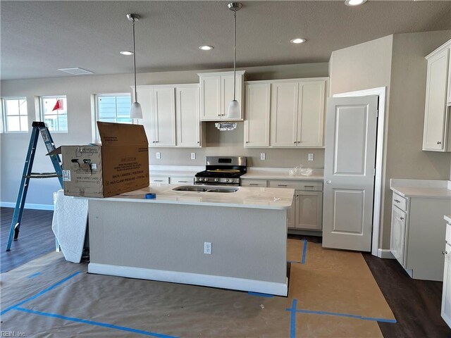 kitchen with a sink, a center island with sink, dark wood-style flooring, and stainless steel range