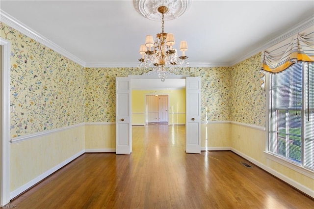 empty room featuring wallpapered walls, a notable chandelier, visible vents, and a wainscoted wall