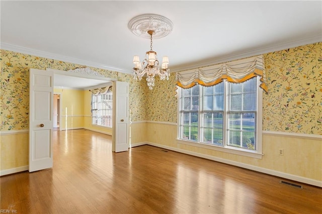 unfurnished room with a wainscoted wall, visible vents, and wallpapered walls